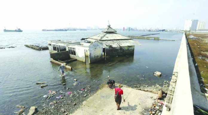 People walk near a giant sea wall which is used as a barrier to prevent sea water from flowing into land and cause flooding in Jakarta, Indonesia, Saturday, July 27, 2019. Indonesia's President Joko Widodo said in an interview that he wants to see the speedy construction of the giant sea wall to save the low-lying capital of Jakarta from sinking under the sea. AP