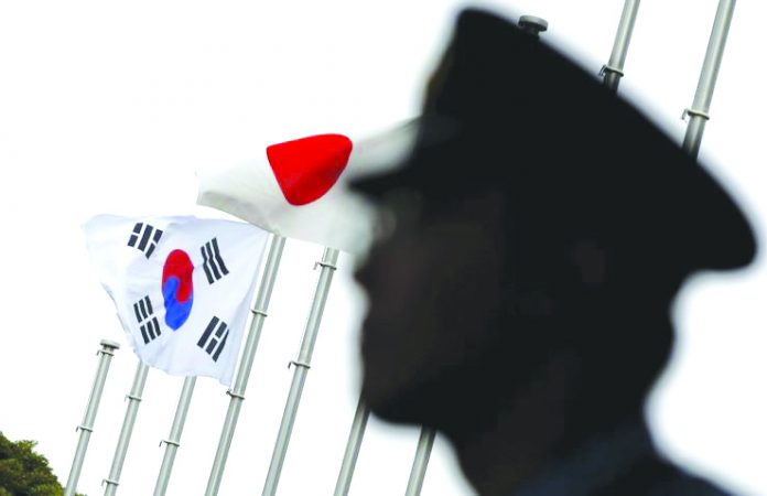 A police officer stands guard near Japanese and South Korean national flags at a hotel, where the South Korean embassy in Japan is holding a reception to mark the 50th anniversary of the normalization of ties between Seoul and Tokyo, in Tokyo, June 22, 2015. REUTERS