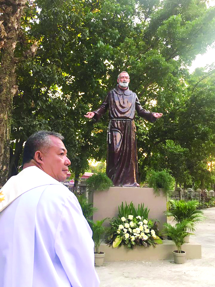 Fr. Jojie Ansula and the statue of St. Padre Pio at the Our Lady of Peace and Good Voyage Parish Church grounds