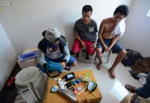 BUSTED DRUG SUSPECTS. Edwin Balinas of Santa Barbara, Iloilo and Janry Napat of Nabas, Aklan look on while an undercover policeman in civilian attire (left) checks the items recovered from them inside a house at a residential subdivision in Barangay Jibao-an, Pavia, Iloilo on Aug. 16, 2019. Sachets of suspected shabu valued at P810,000 were seized. IAN PAUL CORDERO/PN