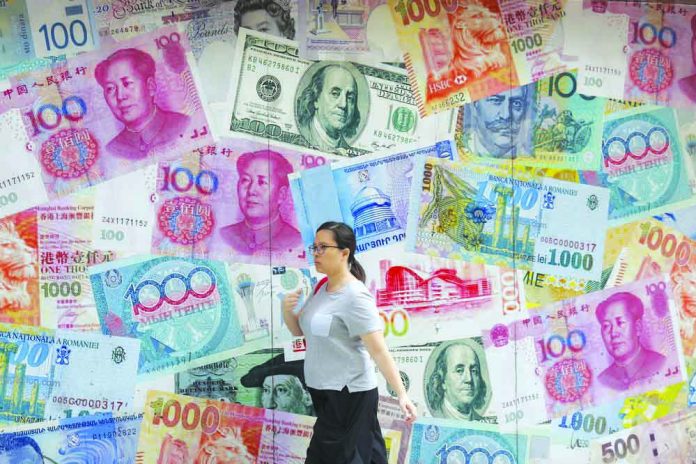 In this Aug. 6, 2019, file photo, a woman walks by a money exchange shop decorated with different countries currency banknotes at Central, a business district in Hong Kong. AP