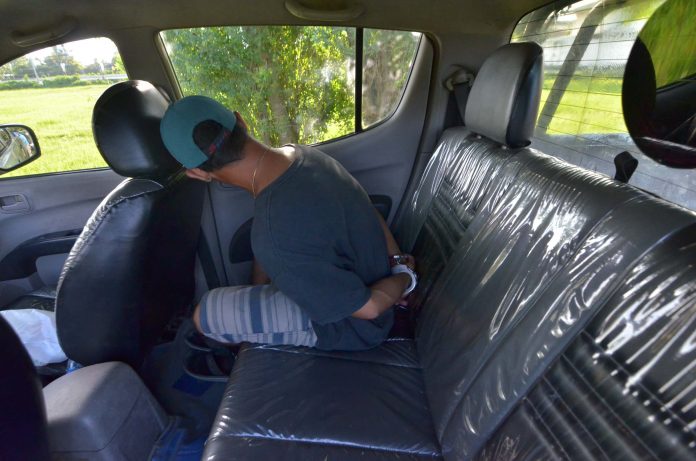 Ramil Abilo sits handcuffed inside a police car after he was arrested in an entrapment operation in Barangay Cabugao Sur, Pavia, Iloilo on Friday. IAN PAUL CORDERO/PN