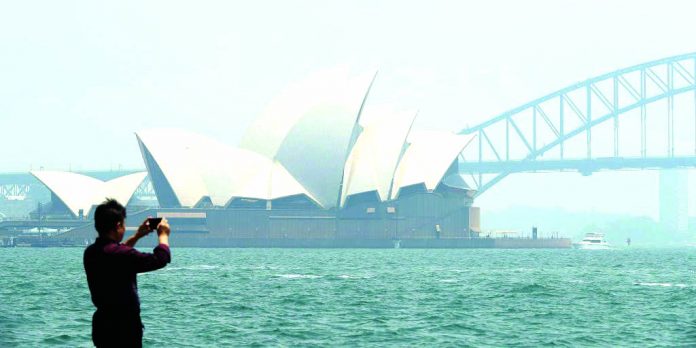 The smoke covered Sydney city Opera House and Harbour Bridge are seen as a man takes a picture at Mrs Macquarie's Chair on Sydney Harbour on Nov. 19, 2019 in Sydney, Australia.GETTY IMAGES