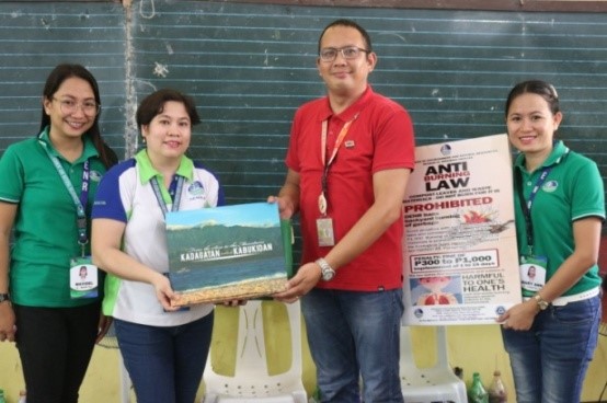 Department of Environment and Natural Resources 6 personnel present the Kadagatan Tubtub Kabukiran coffee table book of Antique congresswoman Loren Legarda and information, education and communication materials to Mr. Sajid Pelayo, principal of Balabag Elementary School.