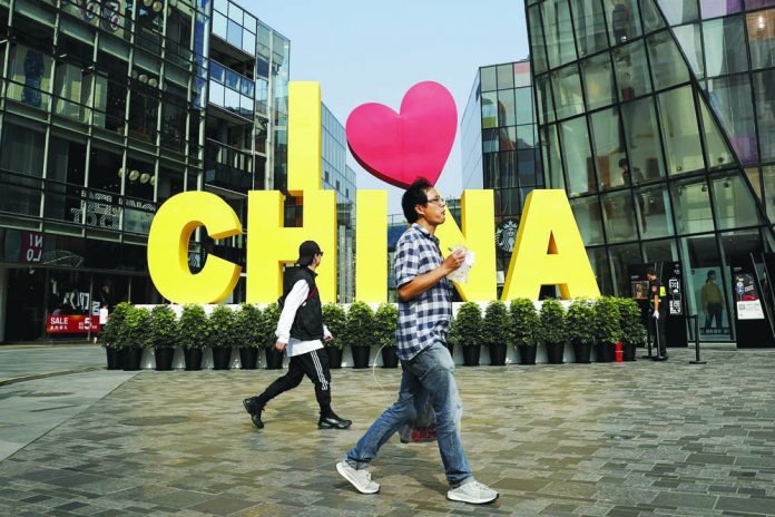 A man eats a snack while passing an “I love China” decoration at a popular shopping mall in Beijing. China put a positive face Saturday on a first-step trade agreement that dials down a trade war it blames the United States for starting. AP