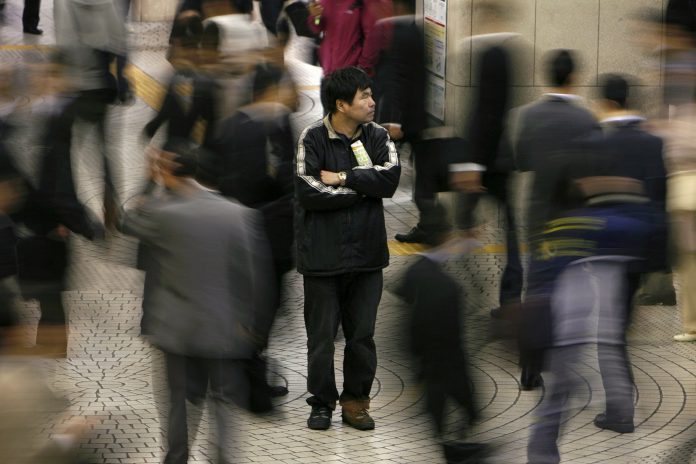 People walk past a man outside Shinjuku train station in Tokyo. REUTERS