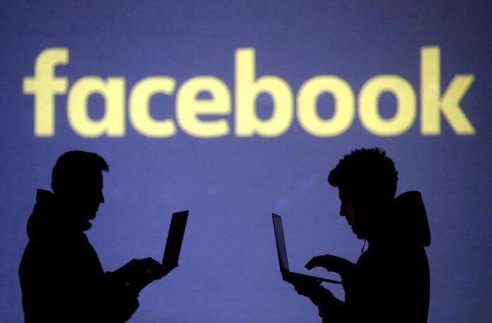 Silhouettes of laptop users are seen next to a screen projection of Facebook logo in this picture illustration taken March 28, 2018. REUTERS/DADO RUVIC/ILLUSTRATION/FILE PHOTO