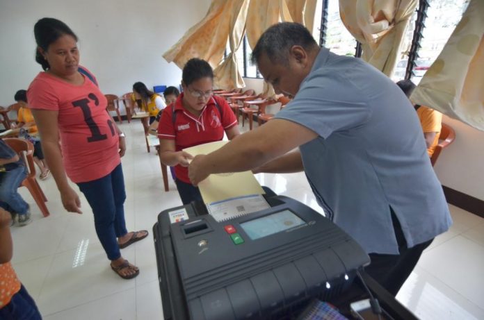 An election officer helps a person with disability feed her ballot into the vote-counting machine during a simulation voting at Central Philippine University in Iloilo City on Jan. 21, 2019. The simulation is a project of the Commission on Elections to further fine-tune the voting processes for persons with disability. IAN PAUL CORDERO/PN