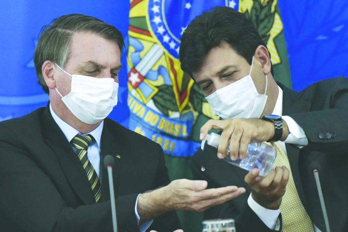 Brazil's Health Minister Luiz Henrique Mandetta, right, gives anti-bacterial gel to President Jair Bolsonaro as they give a press conference on the new coronavirus at Planalto presidential palace in Brasilia, Brazil. AFP