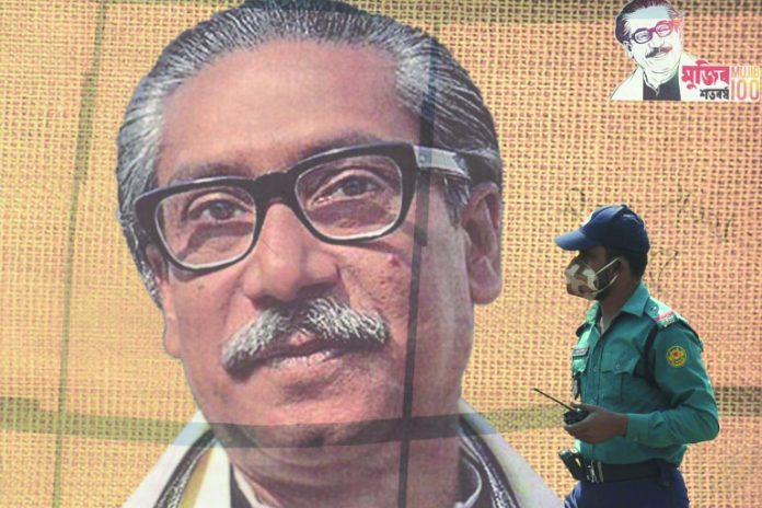 In this file photo taken on March 09, 2020 a policeman wearing a facemask amid fears of the spread of COVID-19 novel coronavirus, walks past a banner with a picture of Bangladesh’s founder Sheikh Mujibur Rahman in Dhaka. AFP