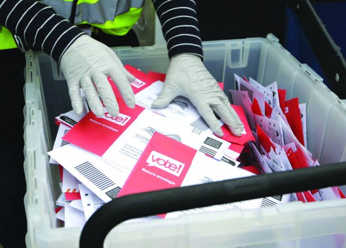 In this March 10, 2020, file photo wearing gloves, a King County Election worker collect ballots from a drop box in the Washington State primary, in Seattle. AP