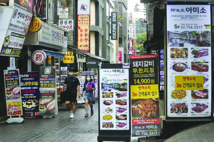 People wearing face masks to help protect against the spread of the coronavirus pass by banners showing the menu items of restaurants in Seoul, South Korea, Friday, Aug. 28, 2020. AP