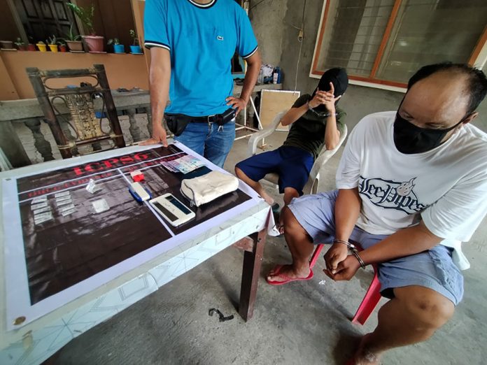 Drug suspects John Winston Porras and Fritz Simbre look on as a police operative presents the items recovered from a buy-bust operation in Barangay Poblacion, Leganes, Iloilo. Porras and Simbre face a charge for violation of the Comprehensive Dangerous Drugs Act of 2002. IAN PAUL CORDERO/ PN