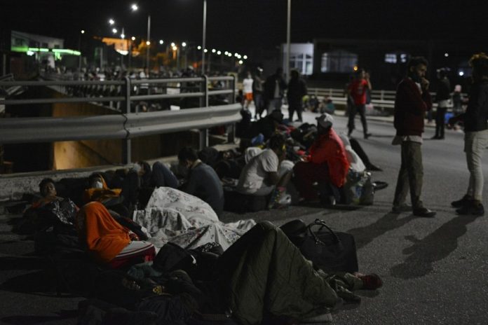 Refugees and migrants gather on a bridge as fire burns at the Moria refugee camp on the northeastern Aegean island of Lesbos, Greece, on Wednesday, Sept. 9, 2020. PANAGIOTIS BALASKAS/AP PHOTO