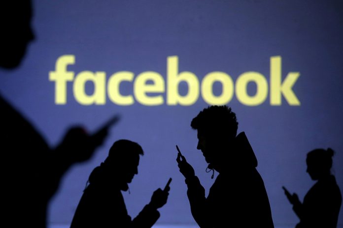 Silhouettes of mobile users are seen next to a screen projection of Facebook logo.DADO RUVIC/REUTERS