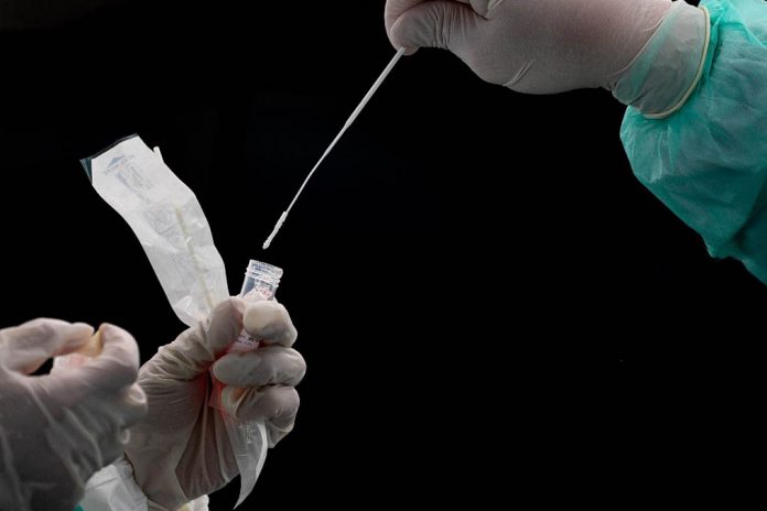 A health worker (R) puts a swab into a tube after collecting a sample for COVID-19 coronavirus testing in Gombak on the outskirts of Kuala Lumpur on April 22, 2020. (Photo by Mohd RASFAN / AFP)