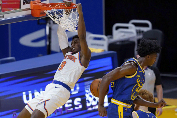 New York Knicks guard RJ Barrett hangs from the rim after dunking next to Golden State Warriors center James Wiseman during the second half of an NBA basketball game on Jan. 21, 2021. JEFF CHIU/AP PHOTO