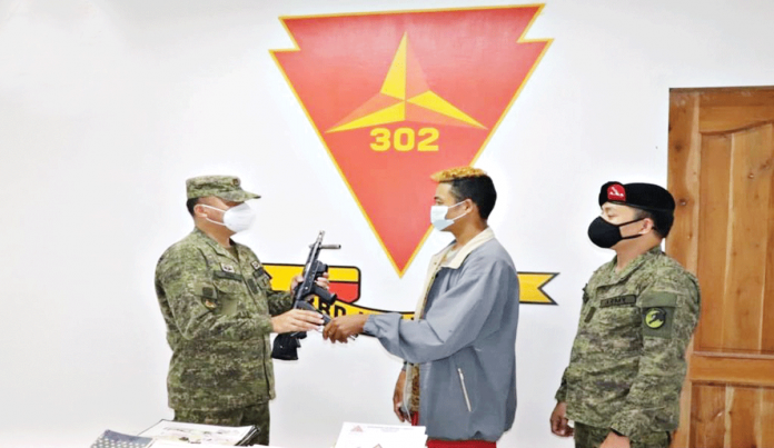 PH ARMY’S 302IB Rebel returnee Jerryd Gargoles turns over a pistol to Colonel Leonardo Pena, commander of the Philippine Army’s 302nd Infantry Brigade in a ceremony in Himalayan City, Negros Occidental.