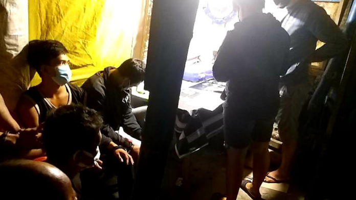 Drug suspects sit handcuffed while police officers inspect items seized from them in a buy-bust operation in Barangay Banago, Bacolod City Tuesday morning./PDEA-6 PHOTO