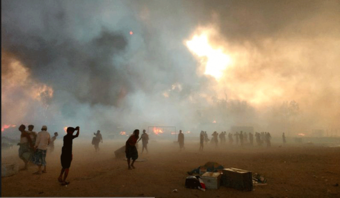 Refugees stand amid smoke after a fire broke out at Rohingya refugee camp in Cox's Bazar, Bangladesh, March 22, 2021. REUTERS/STRINGER/FILE