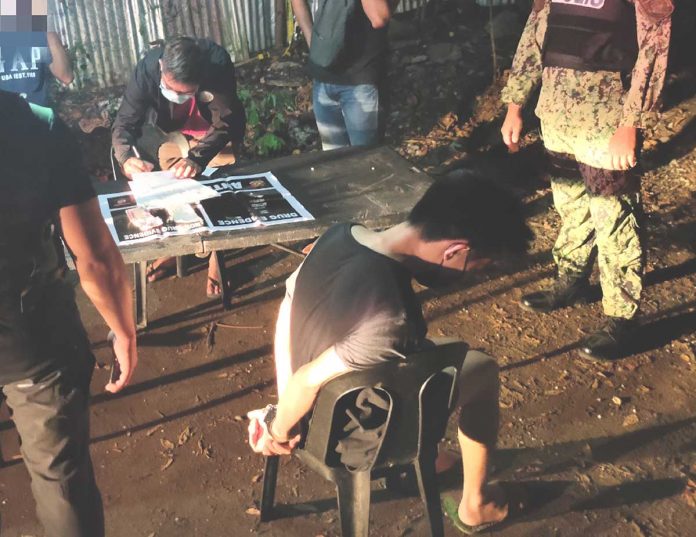 Drug suspect Jan Harry Tating (seated, right foreground) looks away as operatives check the items recovered from him in Barangay 8, San Jose, Antique.