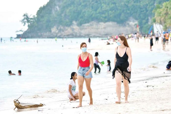 Wearing facemasks, tourists walk barefoot on the white sand of Boracay Beach. Since Aklan is under the modified general quarantine until June 30, leisure travel from the NCR Plus to this province is allowed. MALAY TOURISM OFFICE