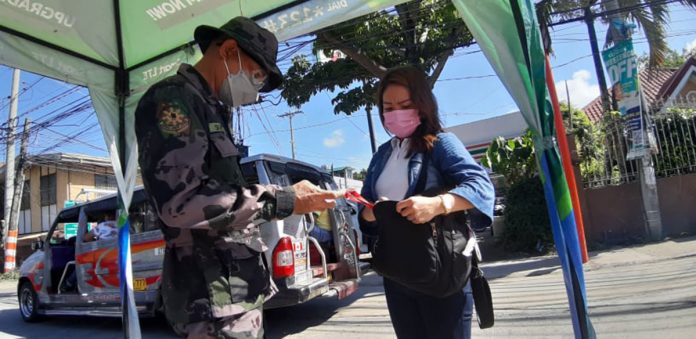 An authorized person outside residence (APOR) presents her travel pass to a police officer at a checkpoint in Barangay Mohon, Arevalo, Iloilo City.