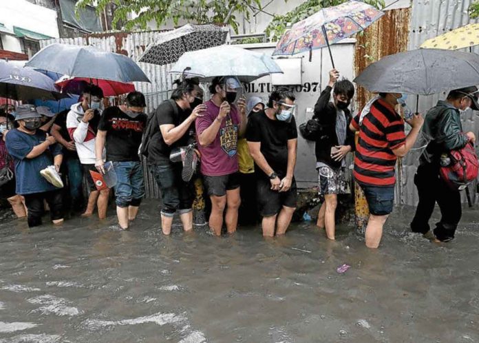 Residents and workers stand in the rain and wade through floodwaters on Wednesday – risking infection from waterborne diseases – just to get into San Andres Sports Complex in Manila, one of the COVID-19 vaccination hubs in the city. RICHARD A. REYES