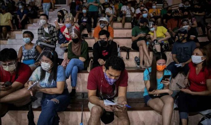 People waiting for their turn at a vaccination site in Manila use their phones to while away time. REUTERS