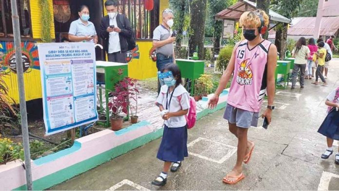 A learner walks with a guardian on the first day of the limited face-to-face classes in Laserna Integrated School in Nabas, Aklan. HERNANI ESCULLAR JR/DEPED-6 PHOTO