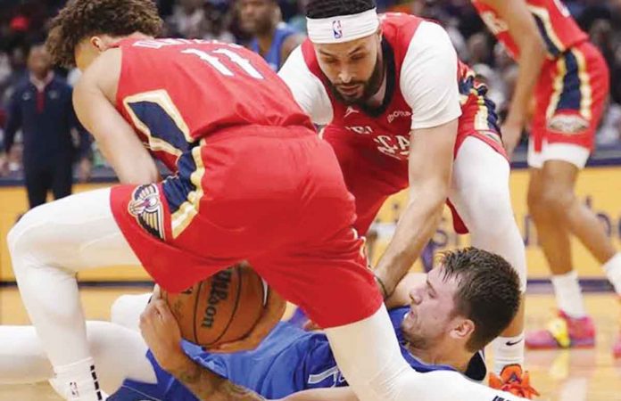 New Orleans Pelicans’ Dyson Daniels (11) and Larry Nance Jr. (in red) gang up on Dallas Mavericks star Luka Doncic (in blue) during a loose ball battle. AP