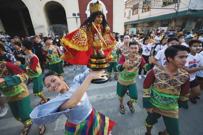 A dancer of a Dinagyang Festival 2023 contesting tribe raises a Sto. Niño image during the Dinagyang “Pamukaw” program in front of the Iloilo City Hall on Dec. 16, 2022. ILOILO CITY MAYOR’S OFFICE PHOTO