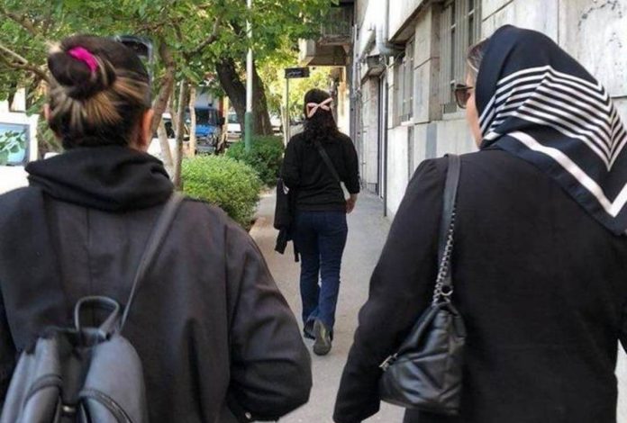 Two women walk down a street, facing away from the camera – one is wearing a headscarf and one is not. Some women in Iran are choosing not to cover their hair as part of ongoing protests. HANDOUT