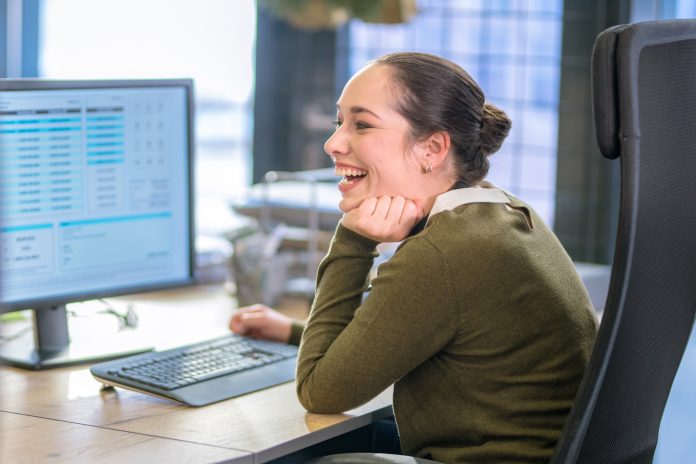 Side view of smiling customer service representative sitting at desk in call centre.