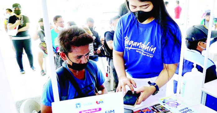 A staff member of a telecommunications firm helps a client register his subscriber identity module card at a stall at the Quezon City Hall. PNA PHOTO BY BEN BRIONES