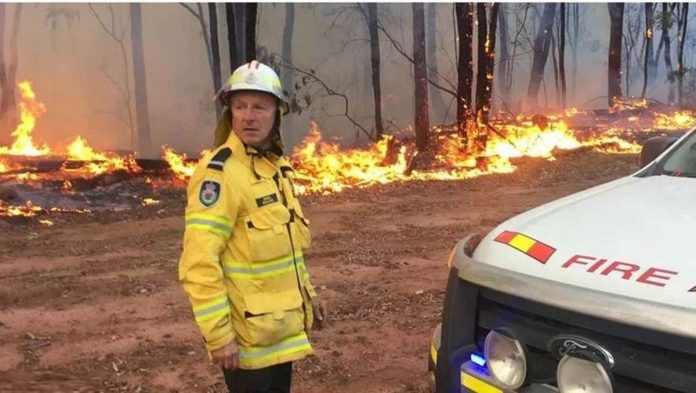 Trees burn behind a fire fighter in Asutralia. There are now over 100 fires across the country. BBC