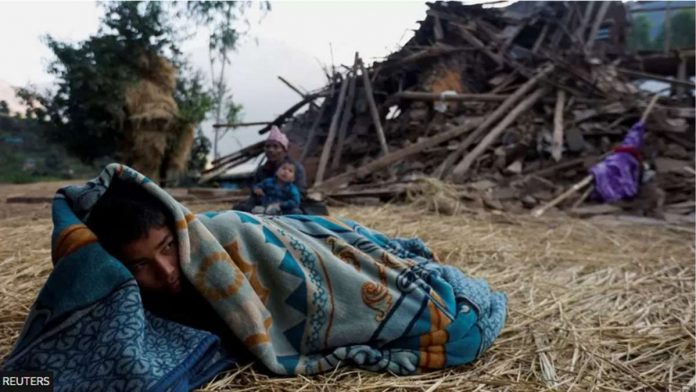 A boy sleeps on the floor next to a house that collapsed during an earthquake in Jajarkot, Nepal. REUTERS