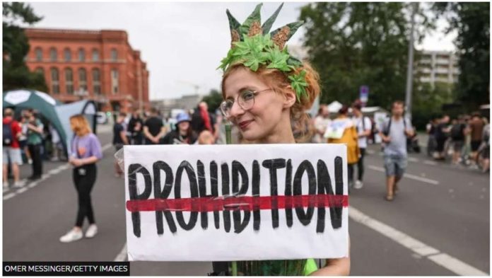 A costumed cannabis supporter holds a banner against prohibition during the annual Hemp Parade on August 12, 2023 in Berlin, Germany. OMER MESSINGER/GETTY IMAGES