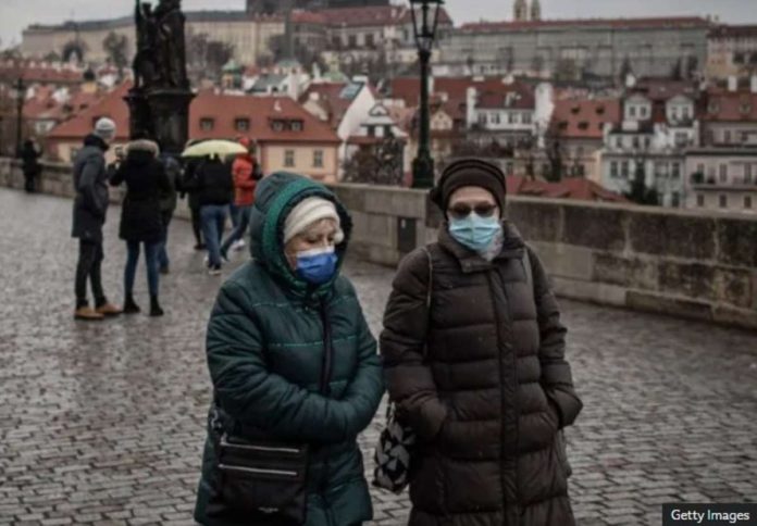 Two women walk side by side in Prague wearing face masks. GETTY IMAGES