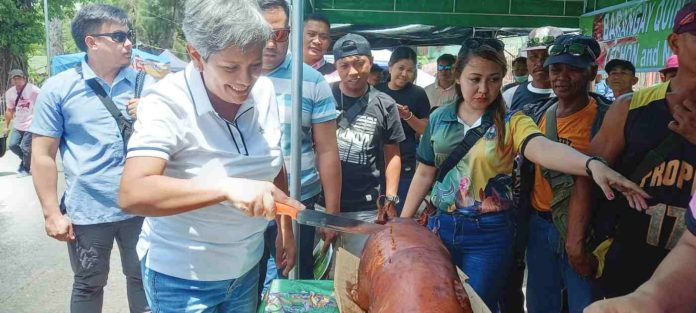 Mayor Ella Celestina Garcia-Yulo of Moises Padilla, Negros Occidental, proudly leads the ceremonial slicing of a lechon (roasted pig), marking the jubilant beginning of the eagerly anticipated free tasting session.