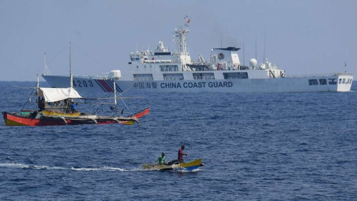 A China Coast Guard ship monitors Philippine fishermen aboard their wooden boats during the distribution of fuel and food to fishers by the civilian-led mission Atin Ito (This Is Ours) Coalition, in the disputed South China Sea on May 16, 2024. A Philippine boat convoy bearing supplies for Filipino fishers said they were headed back to port May 16, ditching plans to sail to a Beijing-held reef off the Southeast Asian country after one of their boats was “constantly shadowed” by a Chinese vessel. Ted Aljibel/Agence France-Presse