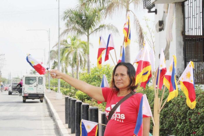 Vendors Jike Nava, Loredil Ariola, and Jerry Potato sell miniature Philippine flags on the bustling streets of Iloilo City, embodying the patriotic spirit of Independence Day. Of course, they wish of brisk sales. They say independence should also be synonymous with economic freedom and opportunities for all Filipinos. AJ PALCULLO/PN