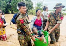 Two soldiers carry an elderly woman in a bucket as they wade through knee-deep muddy water. Behind them several other civilians, carrying children, make their way through the flooding as well. GETTY IMAGES