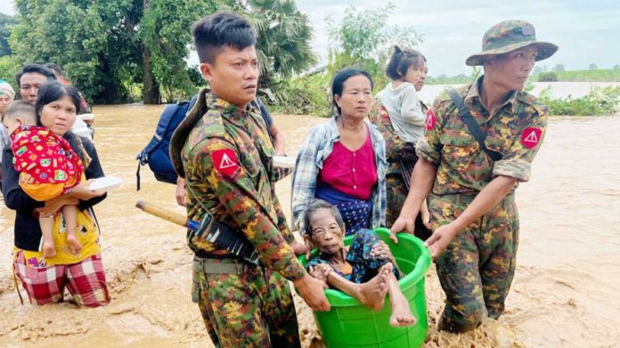 Two soldiers carry an elderly woman in a bucket as they wade through knee-deep muddy water. Behind them several other civilians, carrying children, make their way through the flooding as well. GETTY IMAGES