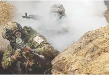 Two Ukrainian soldiers moving through a trench during a chemical weapons training drill. They both have gas masks on and one is partially-obscured by smoke. REUTERS