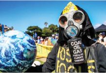 A climate protester wearing a gas mask and protective clothing holds a model of planet earth. The mask reads in captial letters: NO MORE COAL OIL GAS FUELLING CLIMATE CHANGE. GETTY IMAGES