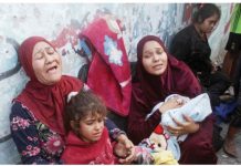 Two women cry out as they lean against a wall and hold two children - one a young girl and the other a baby wrapped in a blanket - in a school sheltering displaced people in Gaza. Another young woman is seen in the background. REUTERS