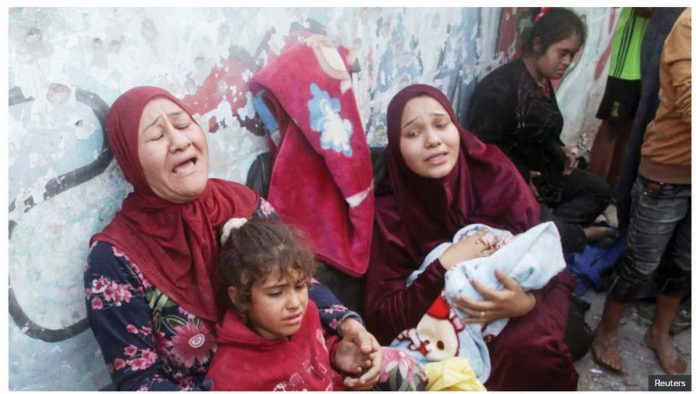 Two women cry out as they lean against a wall and hold two children - one a young girl and the other a baby wrapped in a blanket - in a school sheltering displaced people in Gaza. Another young woman is seen in the background. REUTERS