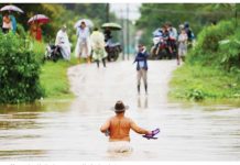 A shirtless man wearing a brown hat and holding his flip flops in one hand wades across waist-deep water while people watch from the other side of an inundated road in El Progreso, Honduras. Many roads and bridges became impassable after days of rain. REUTERS