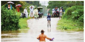 A shirtless man wearing a brown hat and holding his flip flops in one hand wades across waist-deep water while people watch from the other side of an inundated road in El Progreso, Honduras. Many roads and bridges became impassable after days of rain. REUTERS